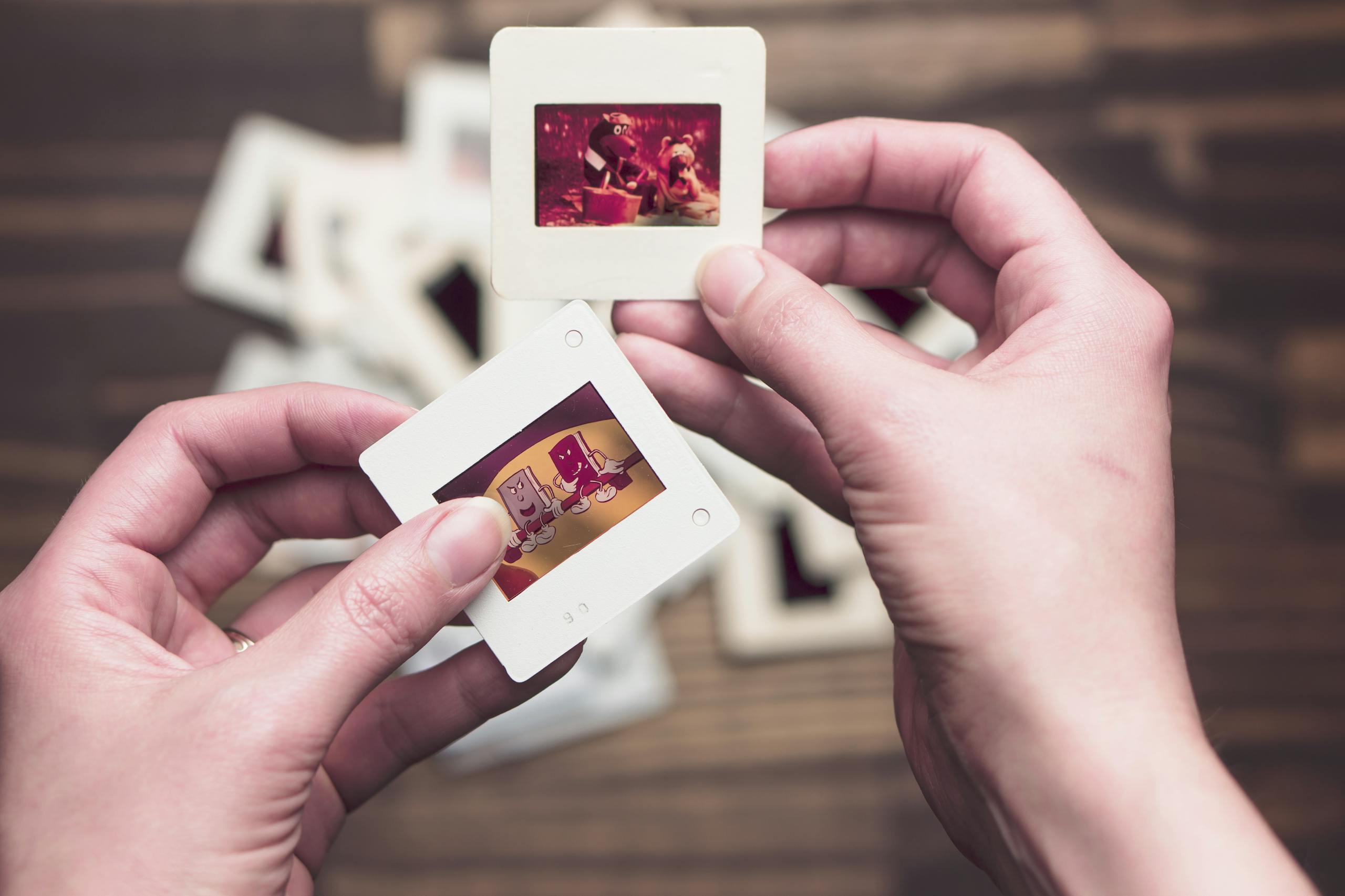 Close-up of hands holding vintage photo slides with faded images on a wooden table background.